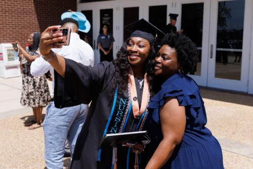 A graduate and a woman lean together for the graduate to a take a selfie on her phone.