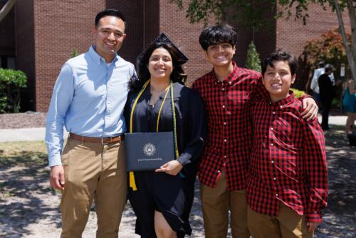 A woman graduate poses with a man and two boys, who are wearing identical red and black plaid shirts, outside the Crown.