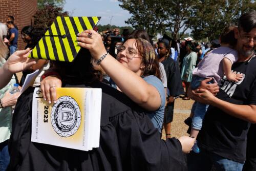 A graduate wearing a decorated cap hugs a woman outside.