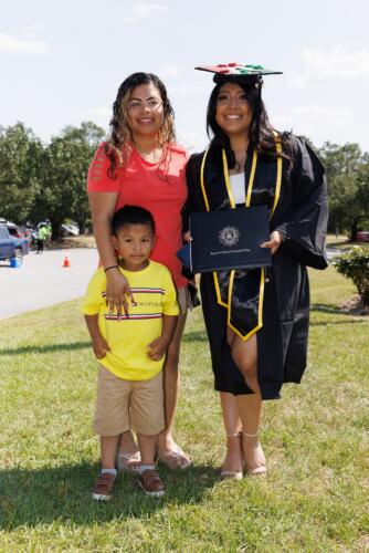 A graduate wearing a decorated cap and a black and gold stole over her gown poses with a woman and young boy.