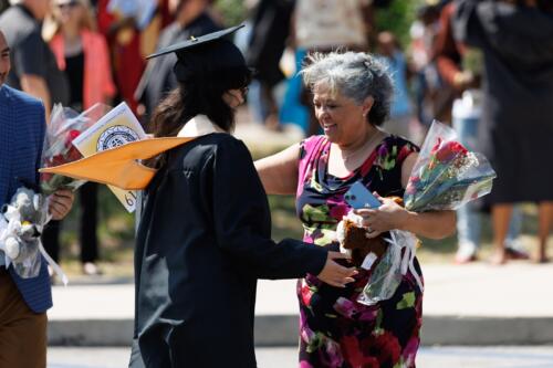 A graduate and a woman walk toward each other to hug.