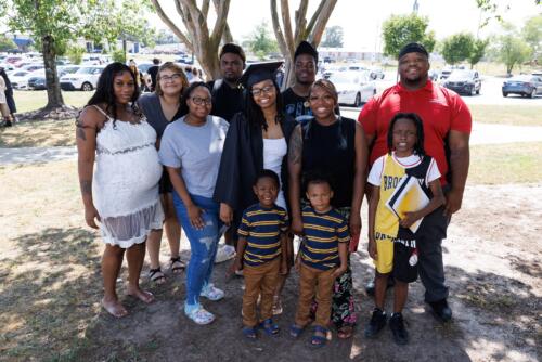 A graduate poses with a group of her loved ones in front of a tree outside of the Crown.