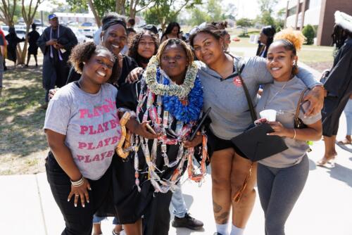 A graduate wearing several leis made of flowers and candy poses with a group of loved ones outside of the Crown.