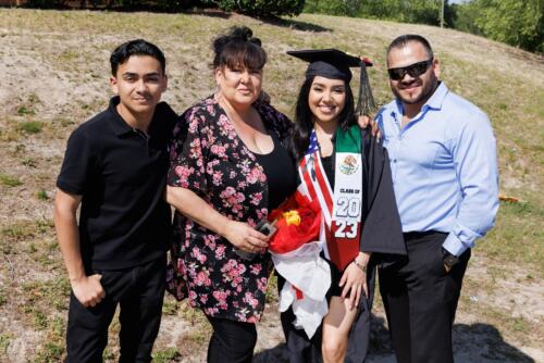 A graduate wearing a stole depicting the flags of the United States and Mexico, poses with her loved ones outside.