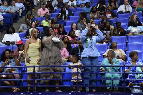 Three woman stand at the railing at the front of the stands. Two of them have their phones up to take pictures.