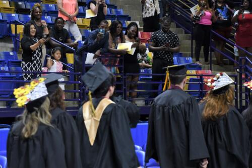 A group of audience members cheers for the graduates, who can be seen from behind in the foreground of the photo.
