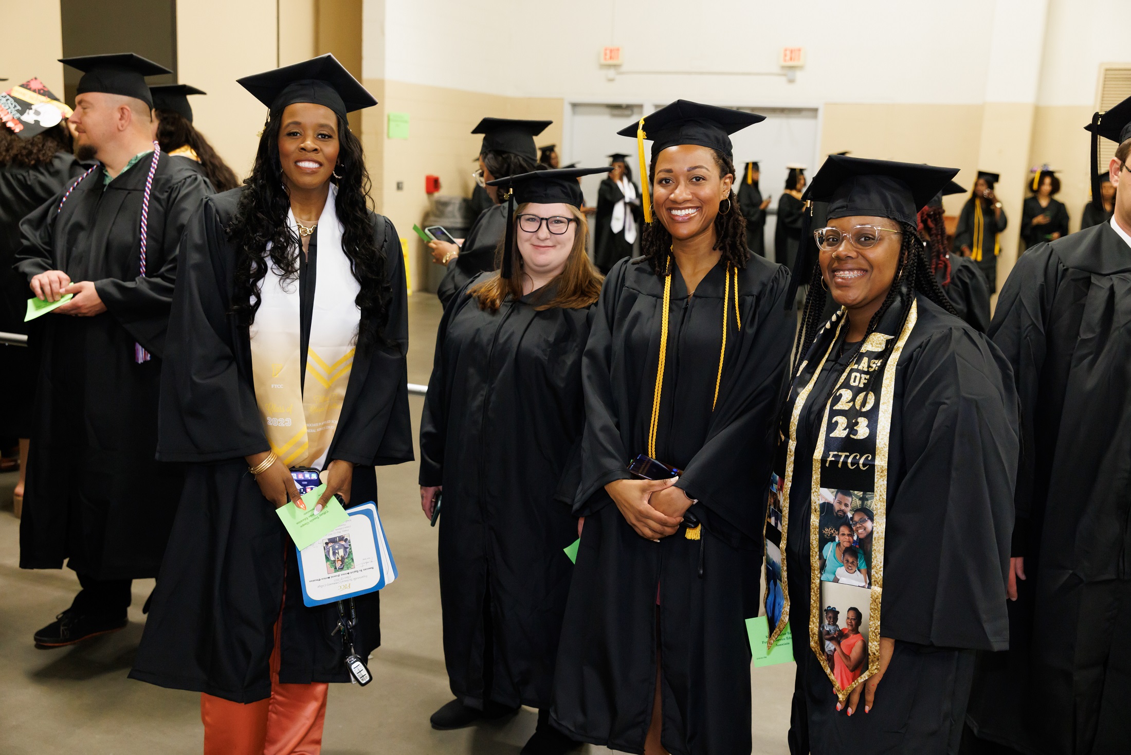 A group of graduates in caps and gowns pose for a photo. Two of them wear stoles.