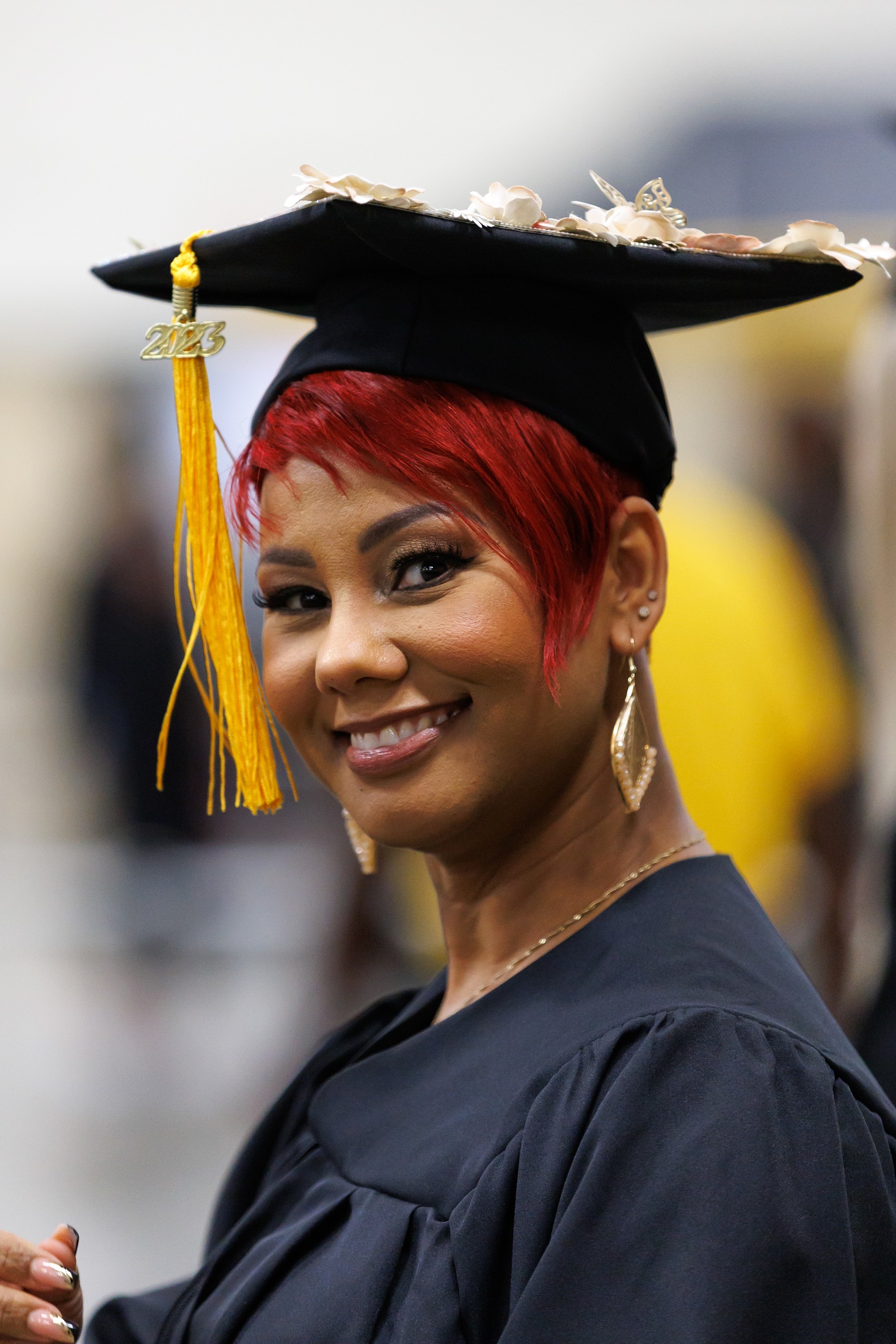 A close-up photo of a graduate with short red hair and dangling gold and pearl earrings smiling at the camera.