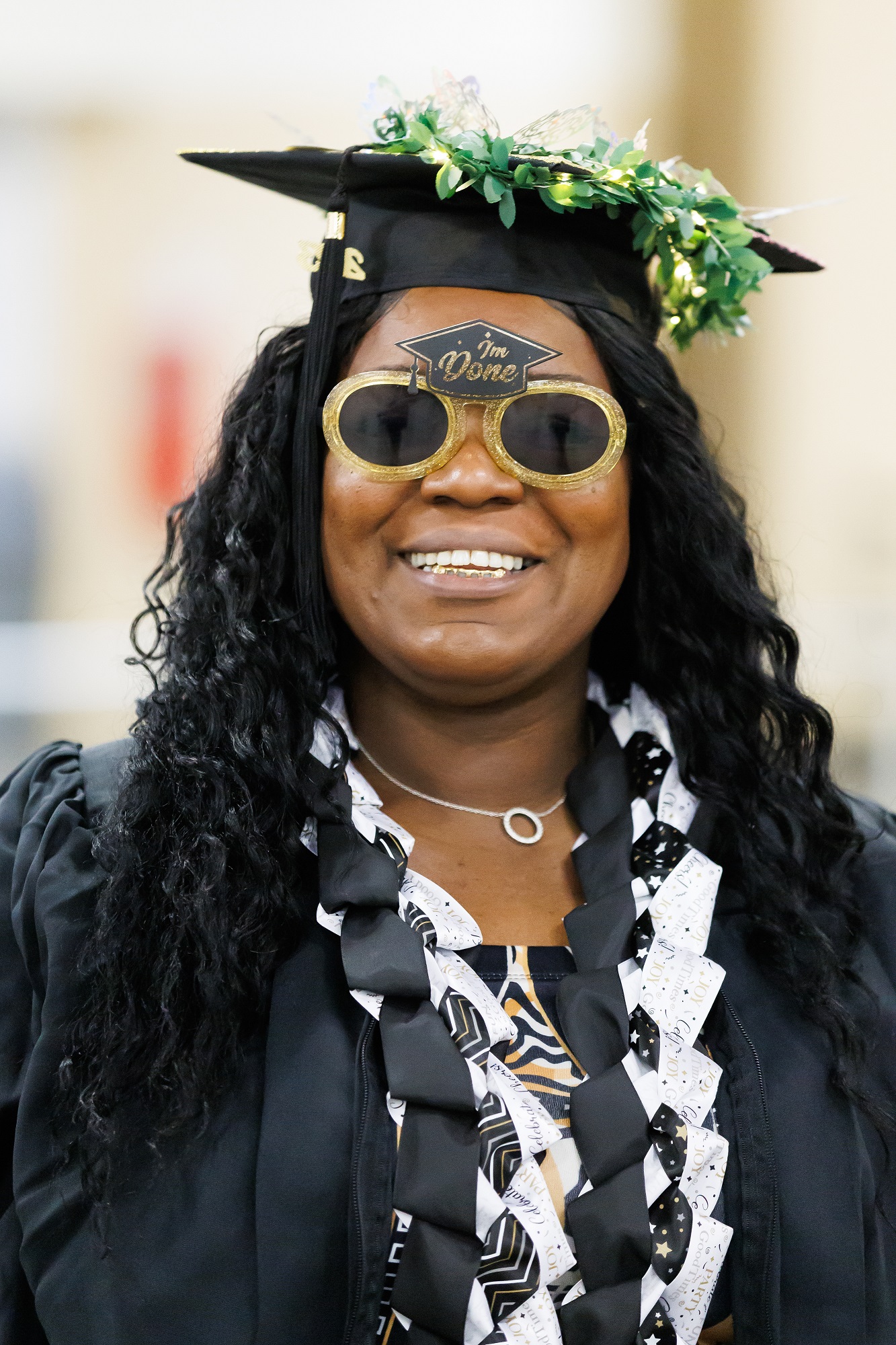 A graduate wears gold sunglasses that have a small mortarboard at the top of the frame with the words "I'm done" written on it.