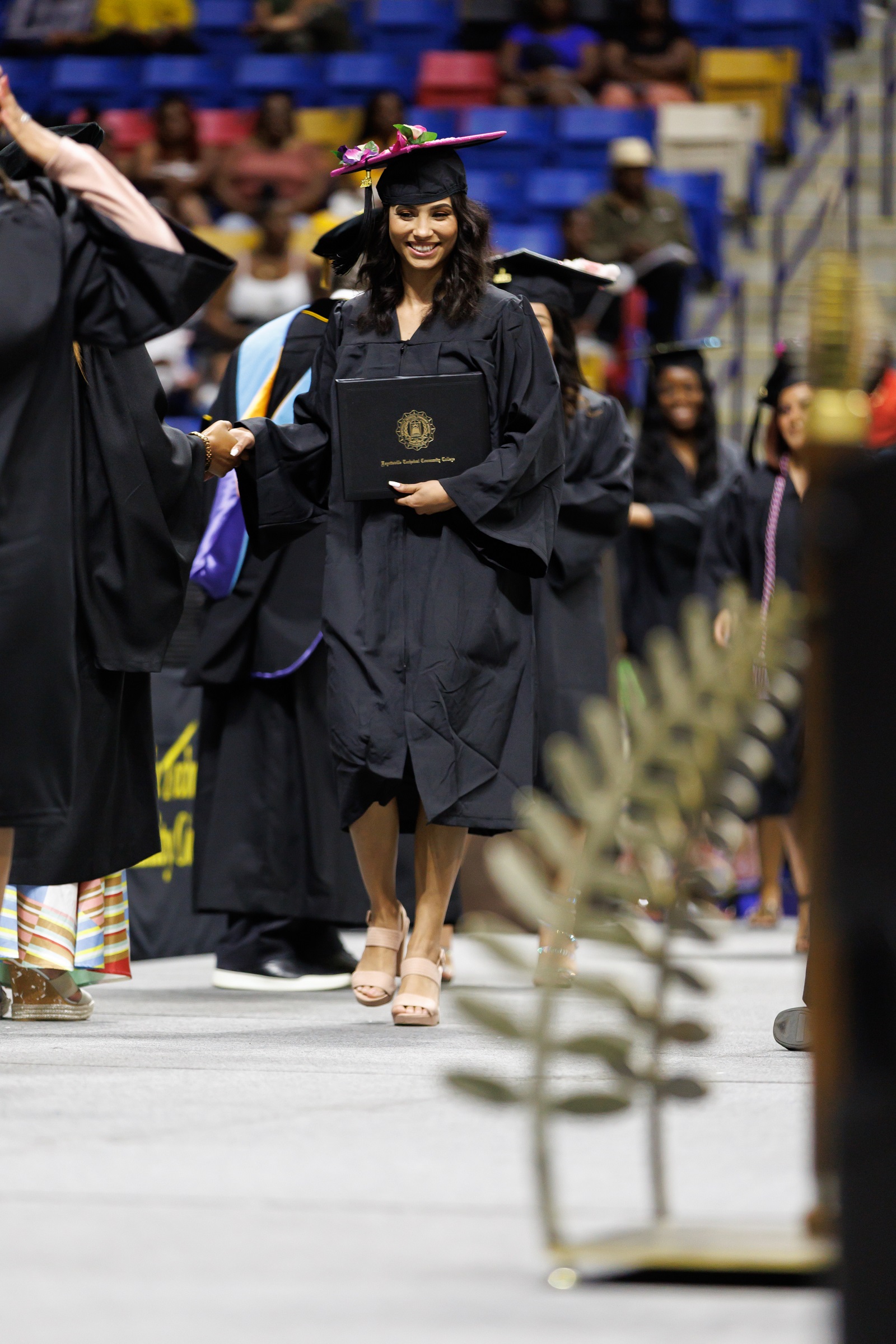 A graduate with a decorated cap shakes hands with Tammy Thurman as she walks across the stage.