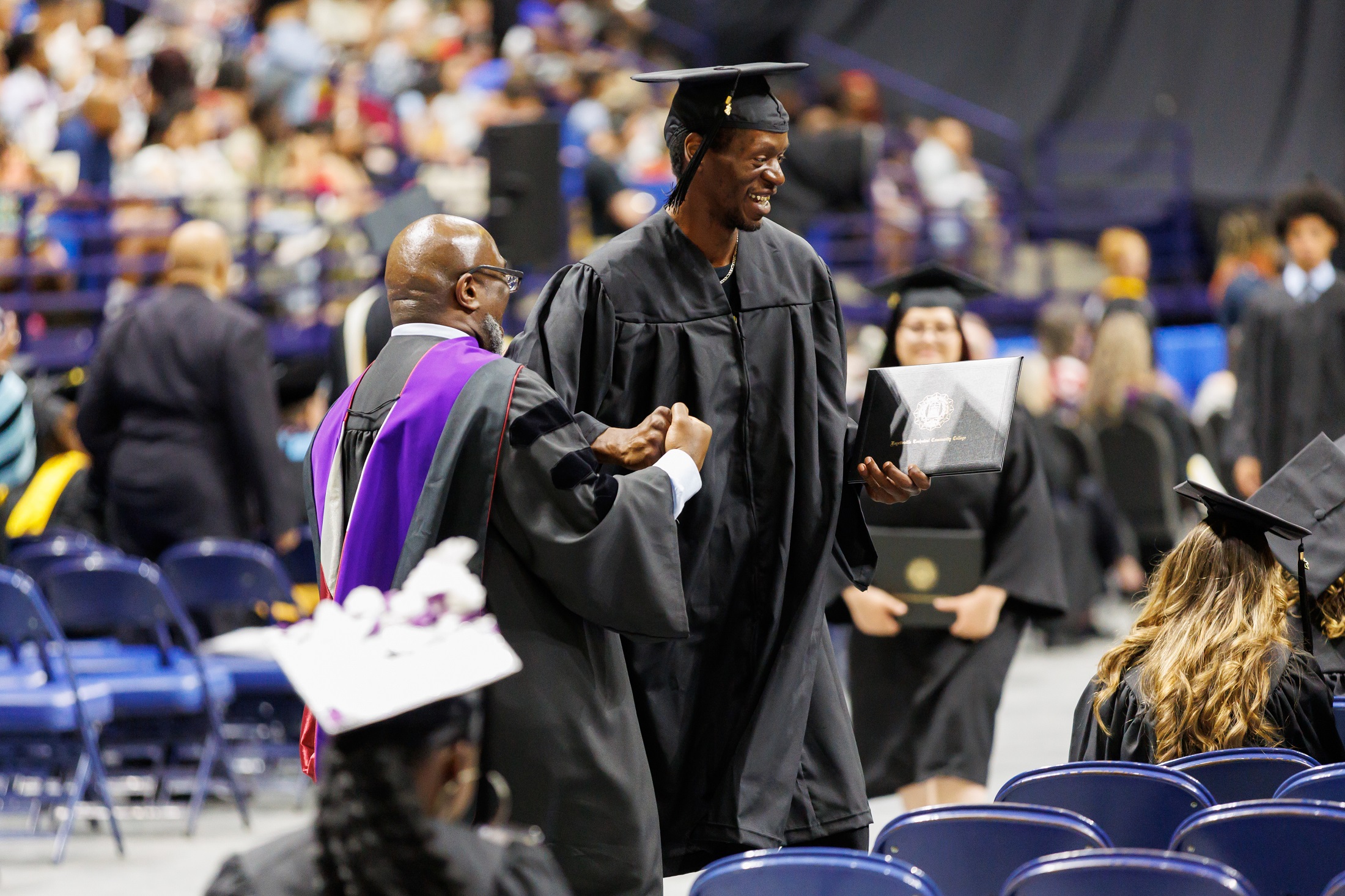A graduate shakes hands with a faculty member as he returns to his seat.