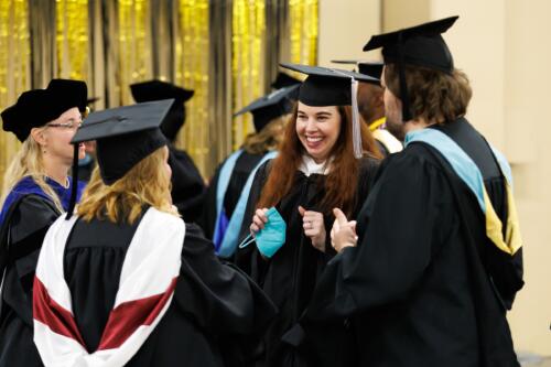 A group of faculty members dressed in regalia talk in the staging area.