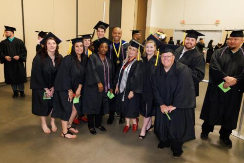 A group of graduates pose with a faculty member in the staging area in the Crown Expo Center.