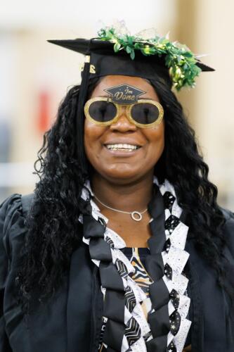 A graduate wears gold sunglasses that have a small mortarboard at the top of the frame with the words "I'm done" written on it.