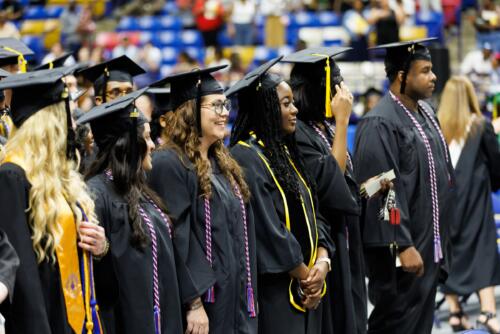 A row of graduates stand in front of their seats.