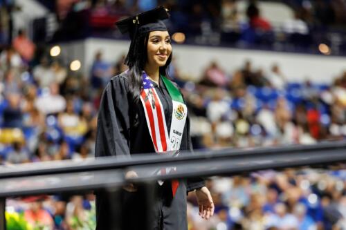 A graduate wearing a stole depicting the flags of the United States and Mexico walks across the stage.