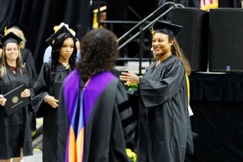 A graduate smiles at a faculty member in front of the stage.