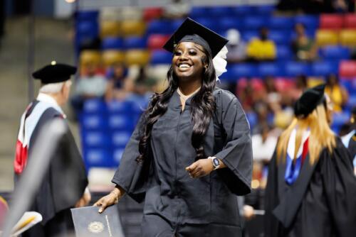 A graduate smiles as a she walks across the stage after receiving her diploma folder.
