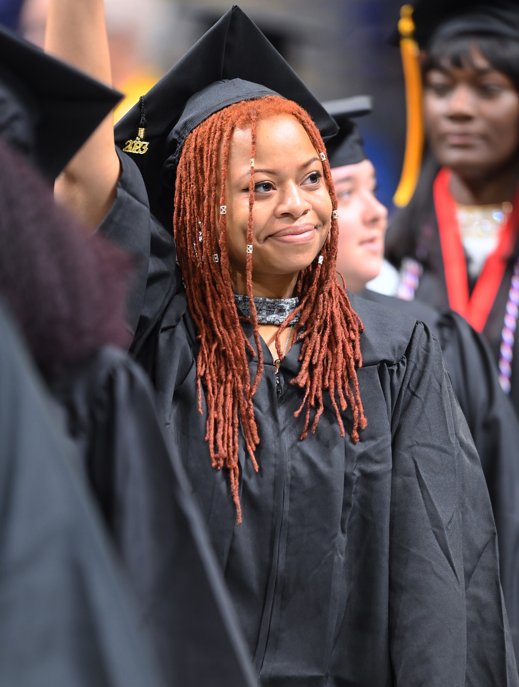 A graduate with long red hair raise her hand and smiles toward the crowd.