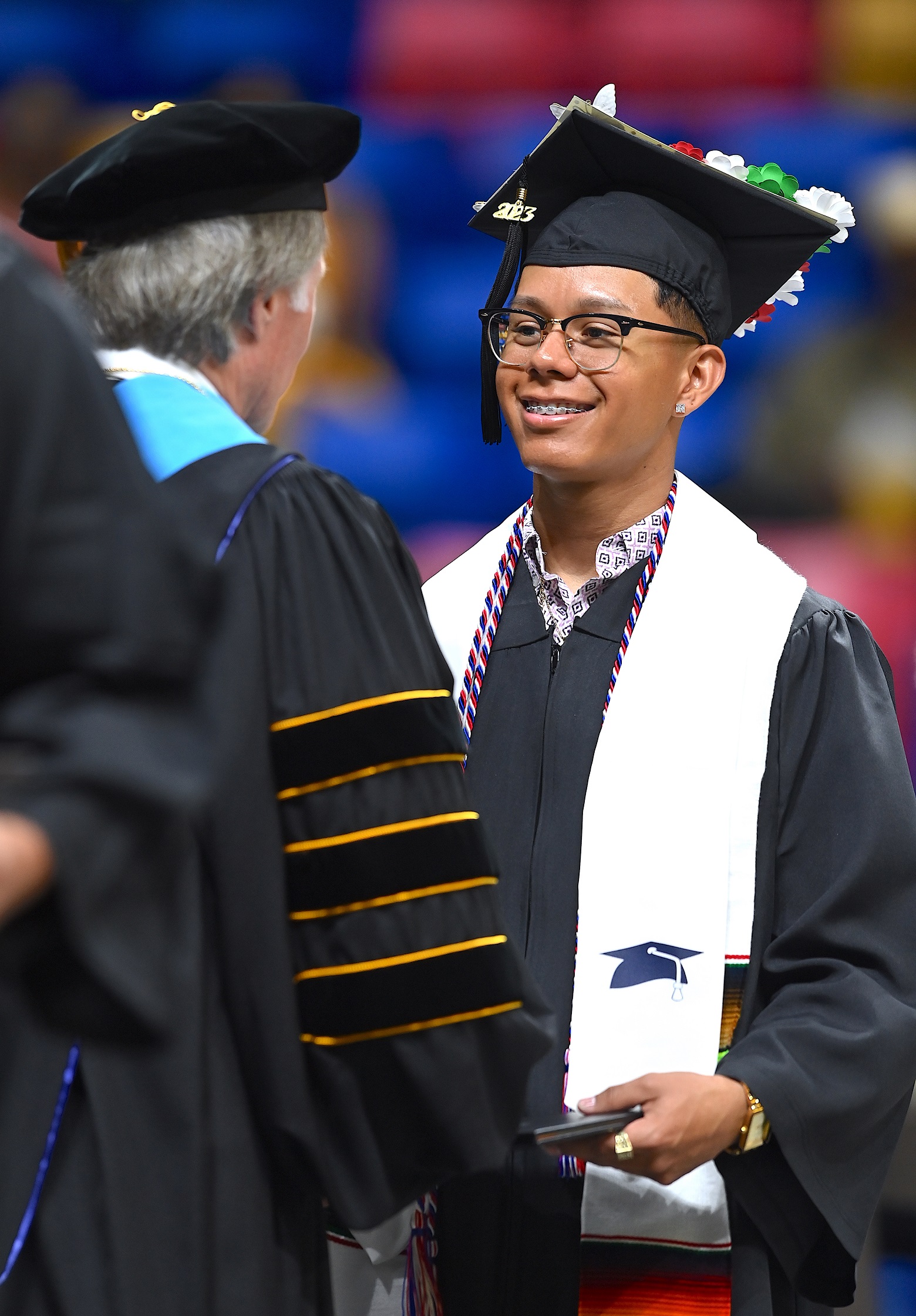 A graduate wearing a white stole with a small cap and tassel on it smiles at Dr. Mark Sorrells.