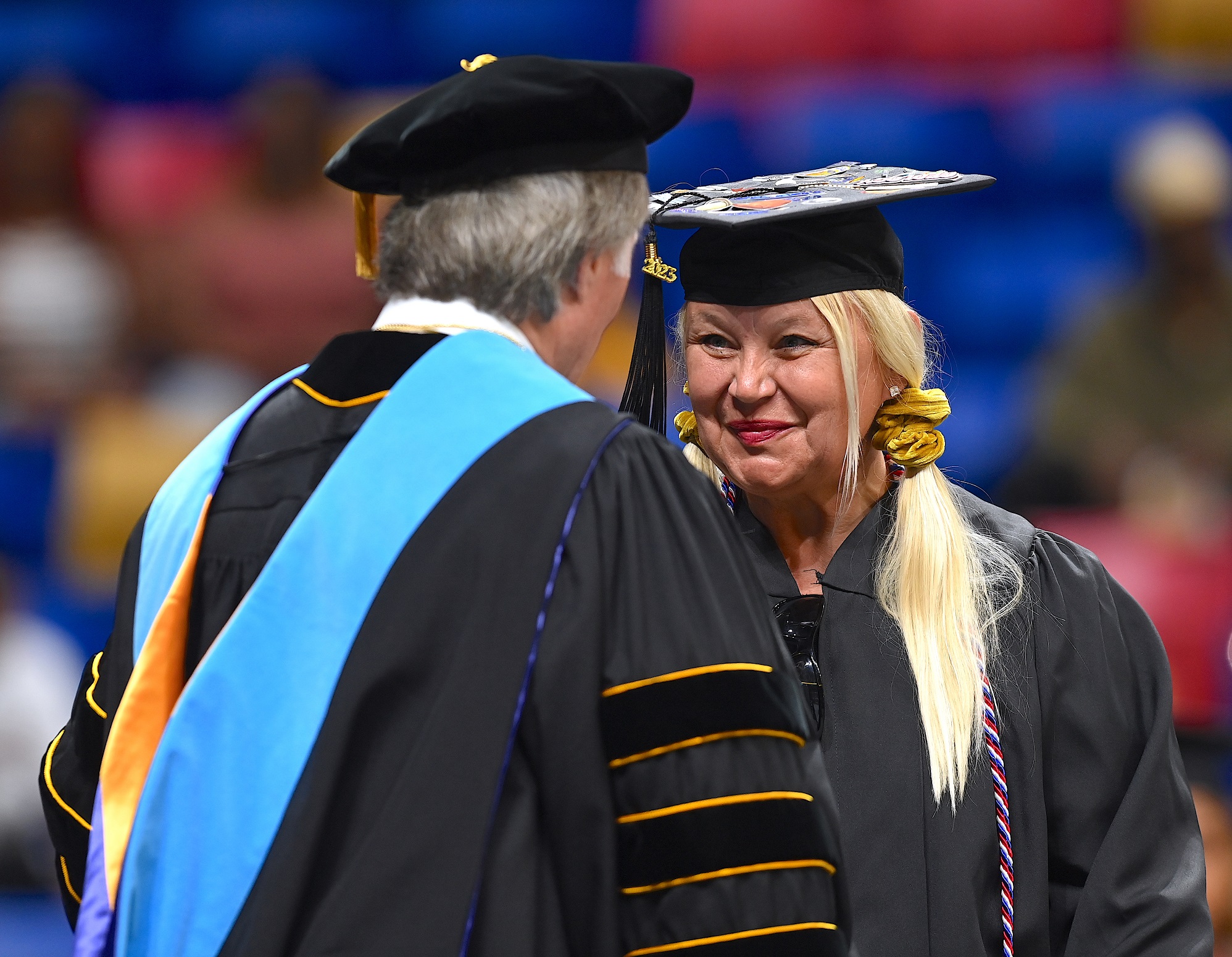 A graduate with a decorated cap smiles at Dr. Mark Sorrells as she accepts her diploma folder.