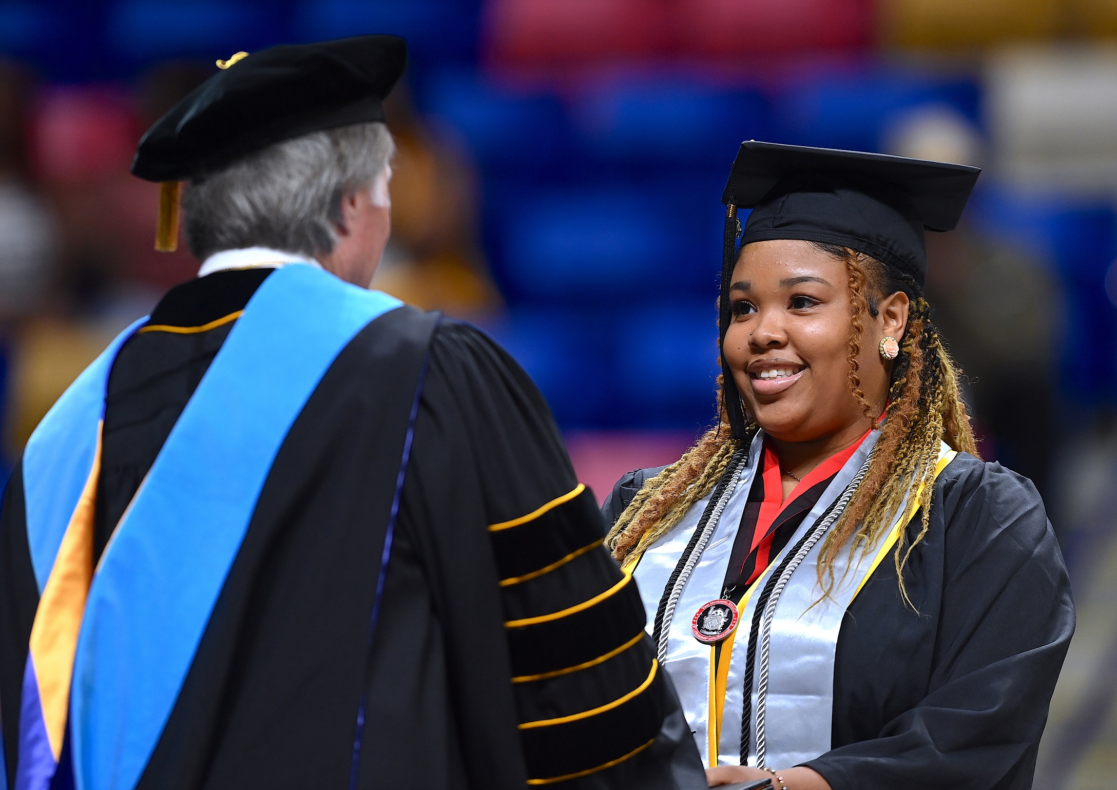 A graduate wearing a light blue stole and a medallion on a red ribbon accepts her diploma folder from Dr. Mark Sorrells.