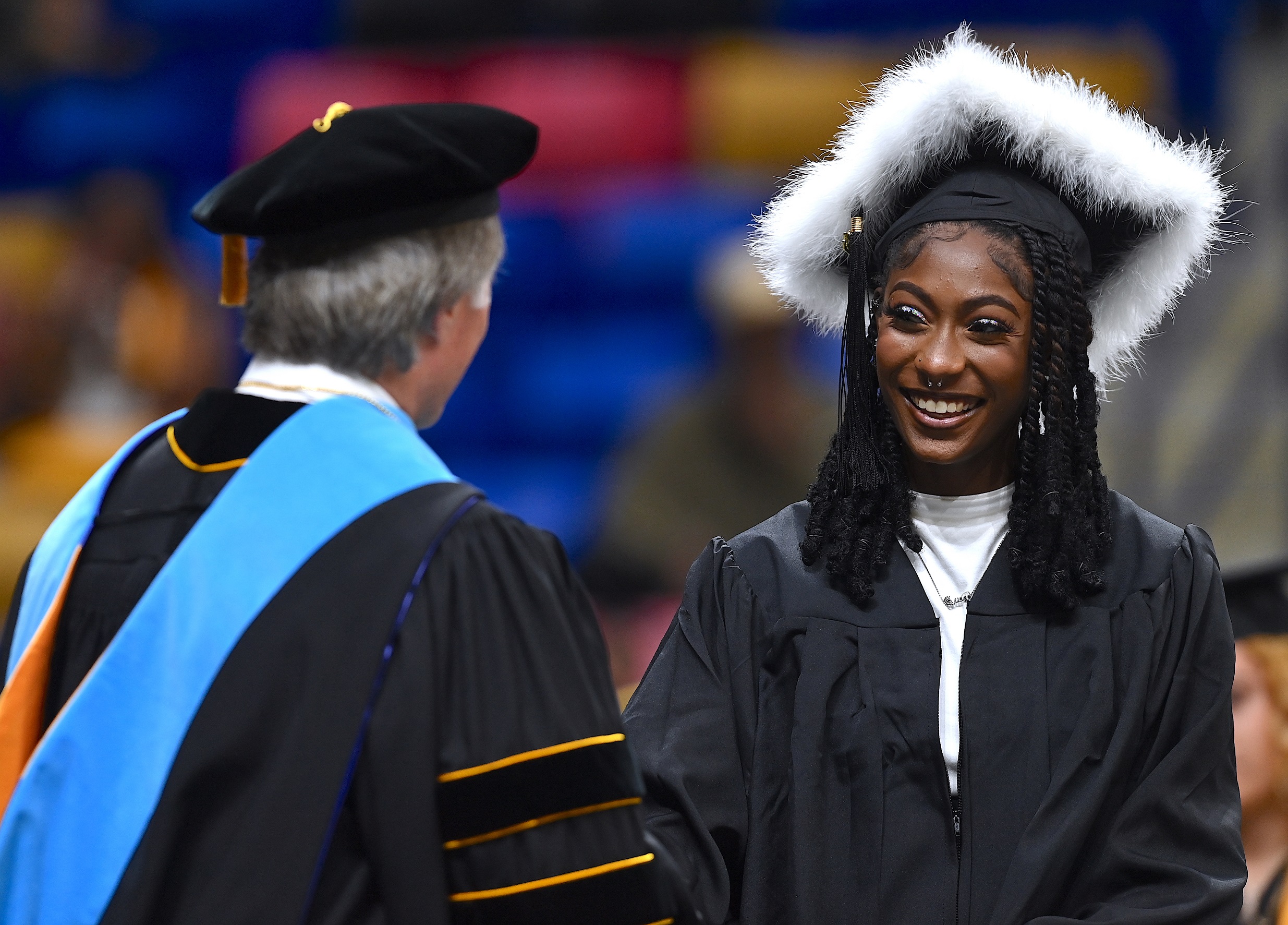 A graduate with a cap trimmed in fur smiles at Dr. Mark Sorrells.