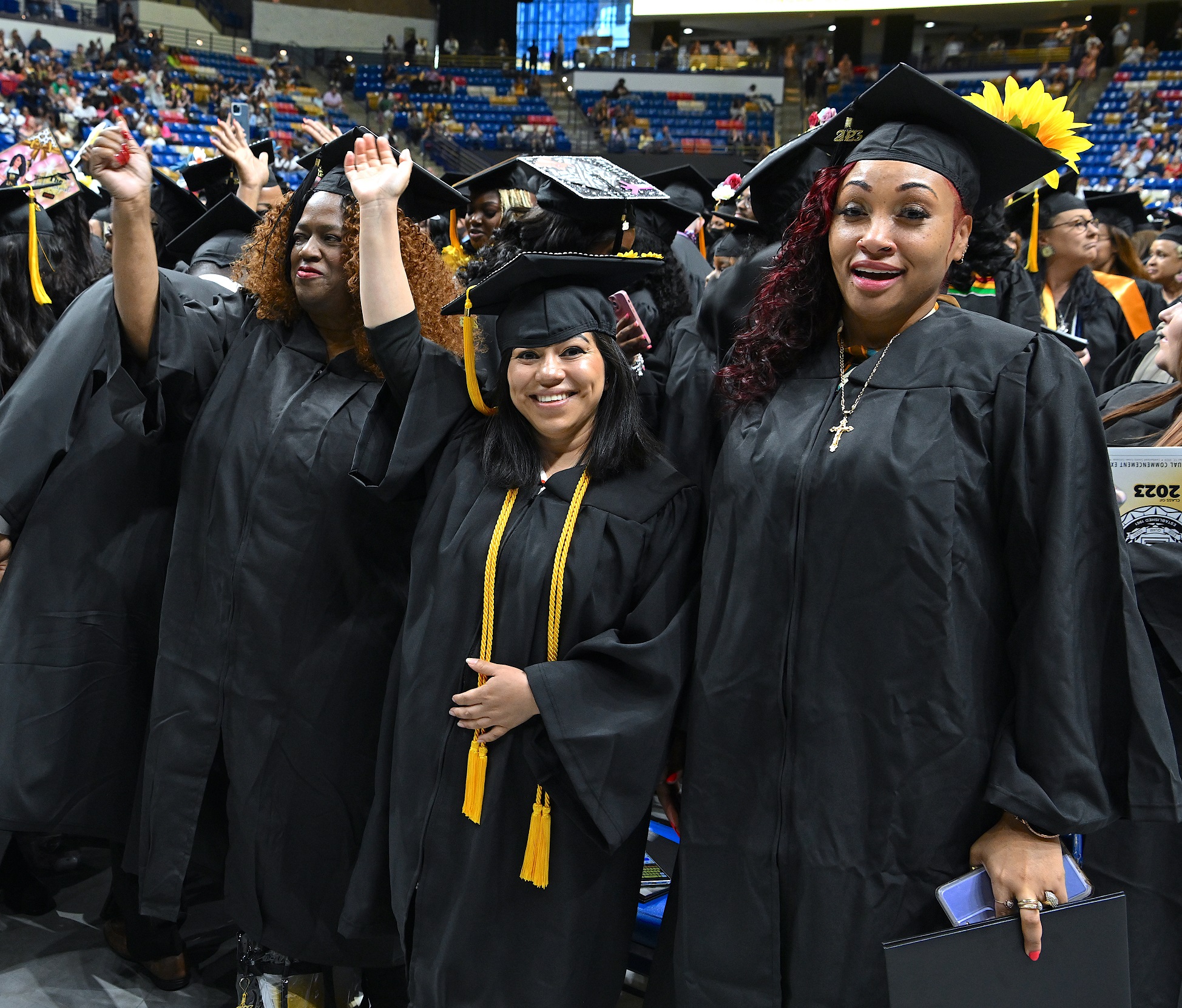 Graduates standing in a row smile and wave at the camera.