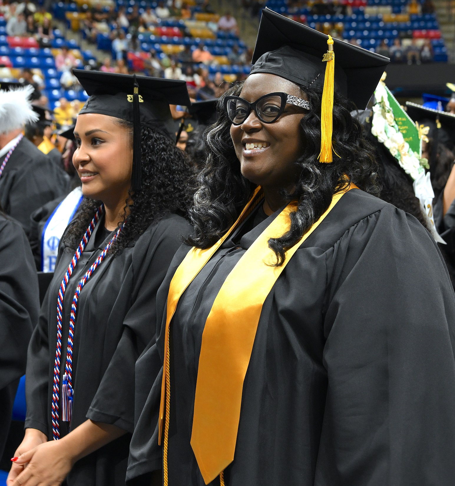 A graduate standing in a row smiles at the camera.