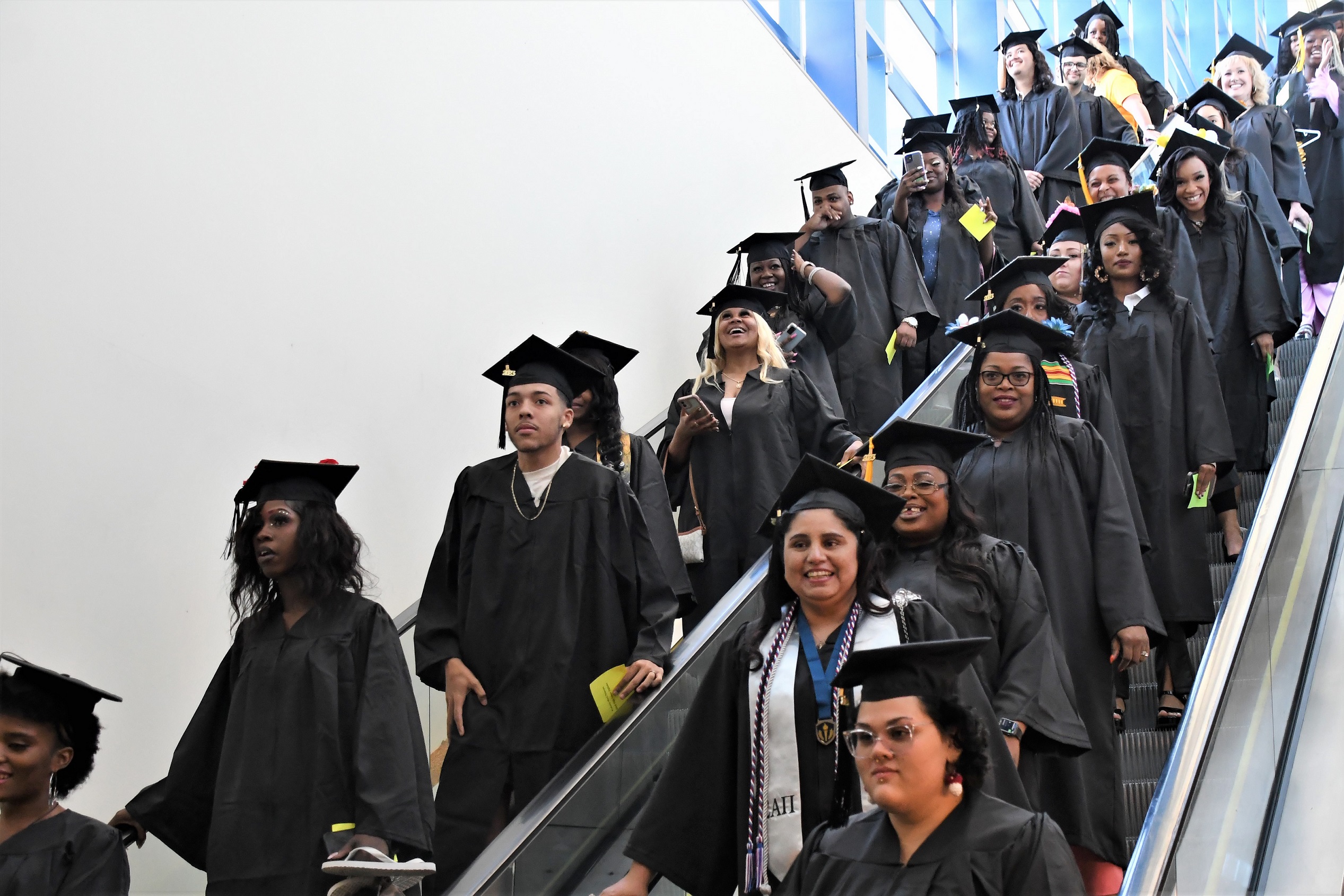 Graduate descend on side-by-side escalators.
