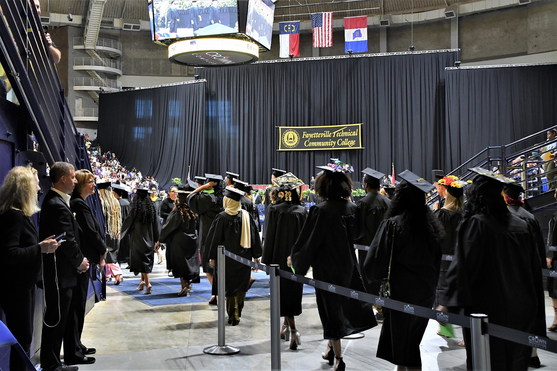 Graduates, shown from behind, walk in processional lines into the Crown.