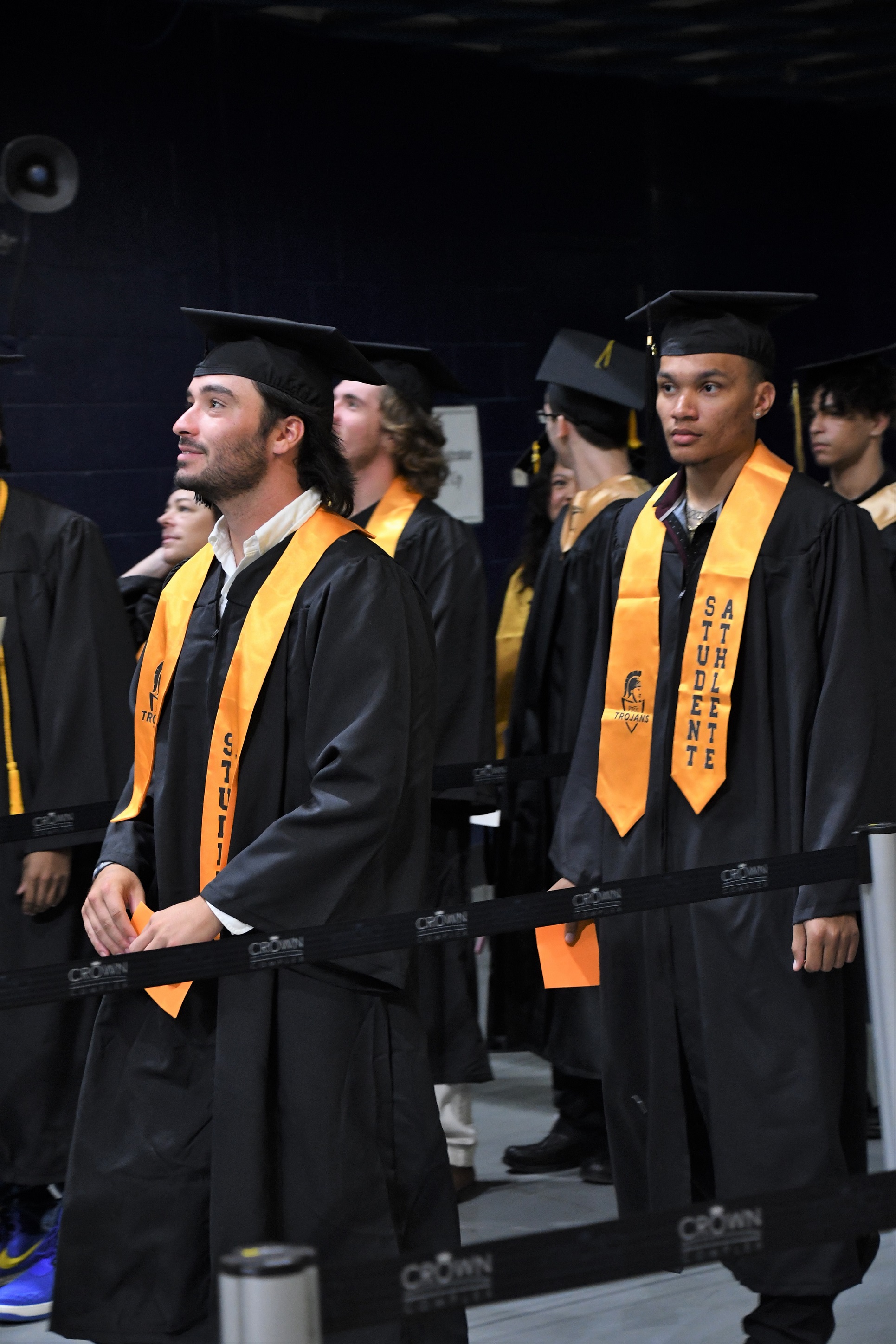 Graduates wearing gold stoles that say "Student Athlete" walk into the Crown.