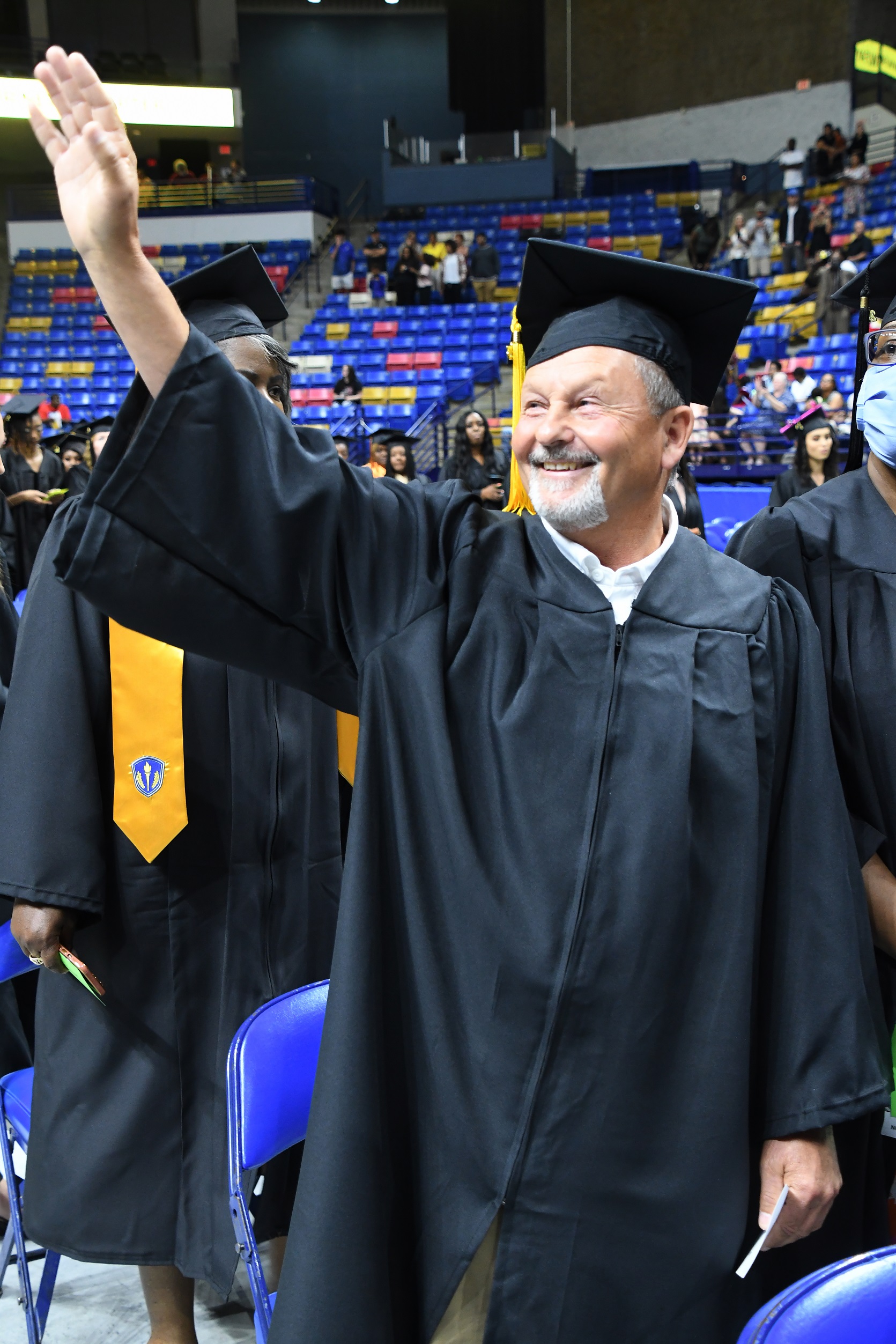 A graduate with a gray goatee waves to the crowd.
