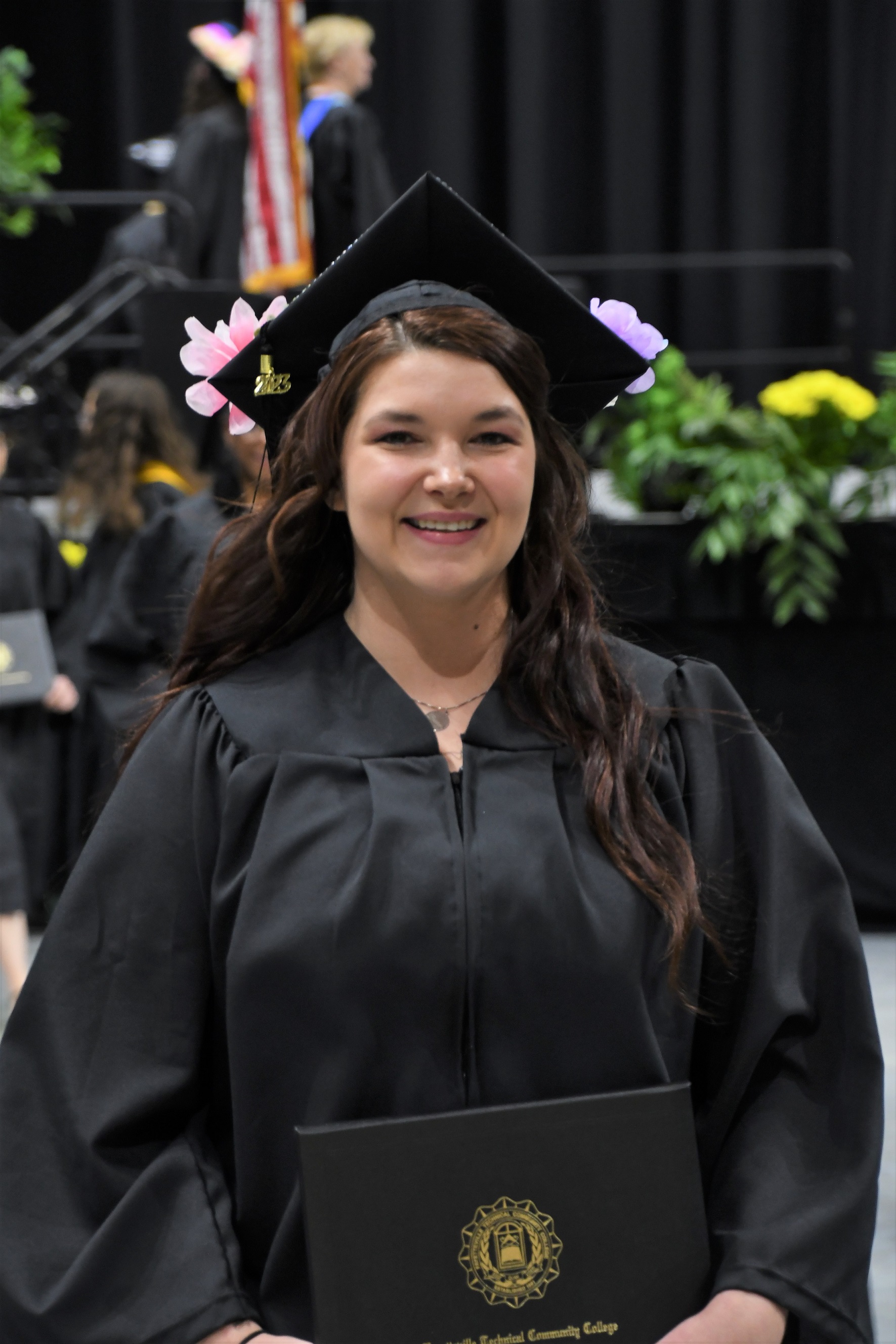 A graduate smiles at the camera as she walks down the aisle.