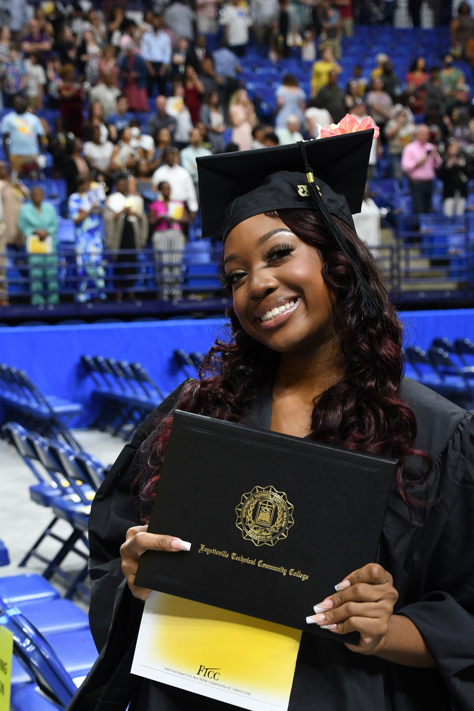 A graduate smiles at the camera and holds up her diploma folder.