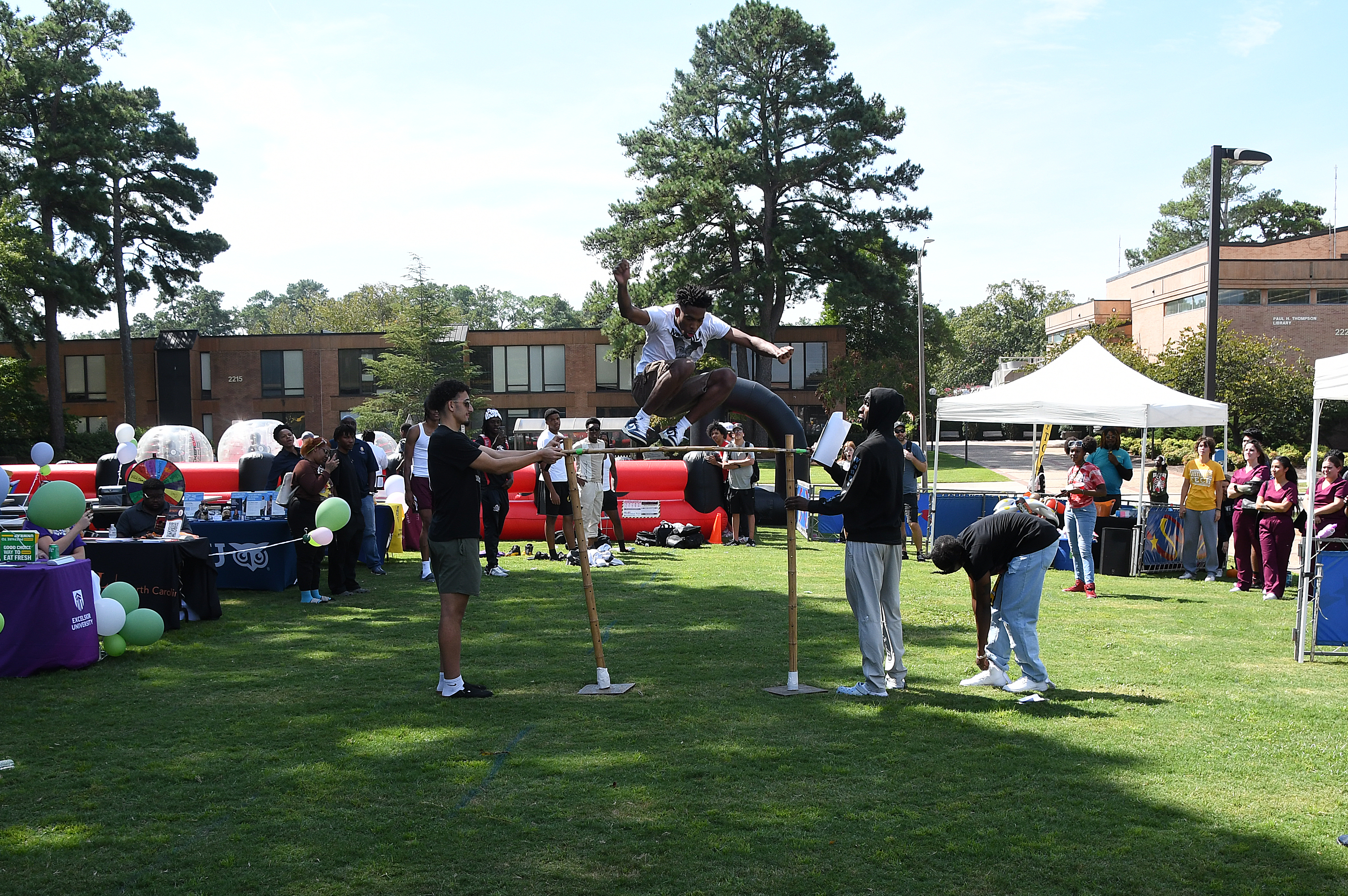 A student jumps over a tall hurdle made of bamboo.