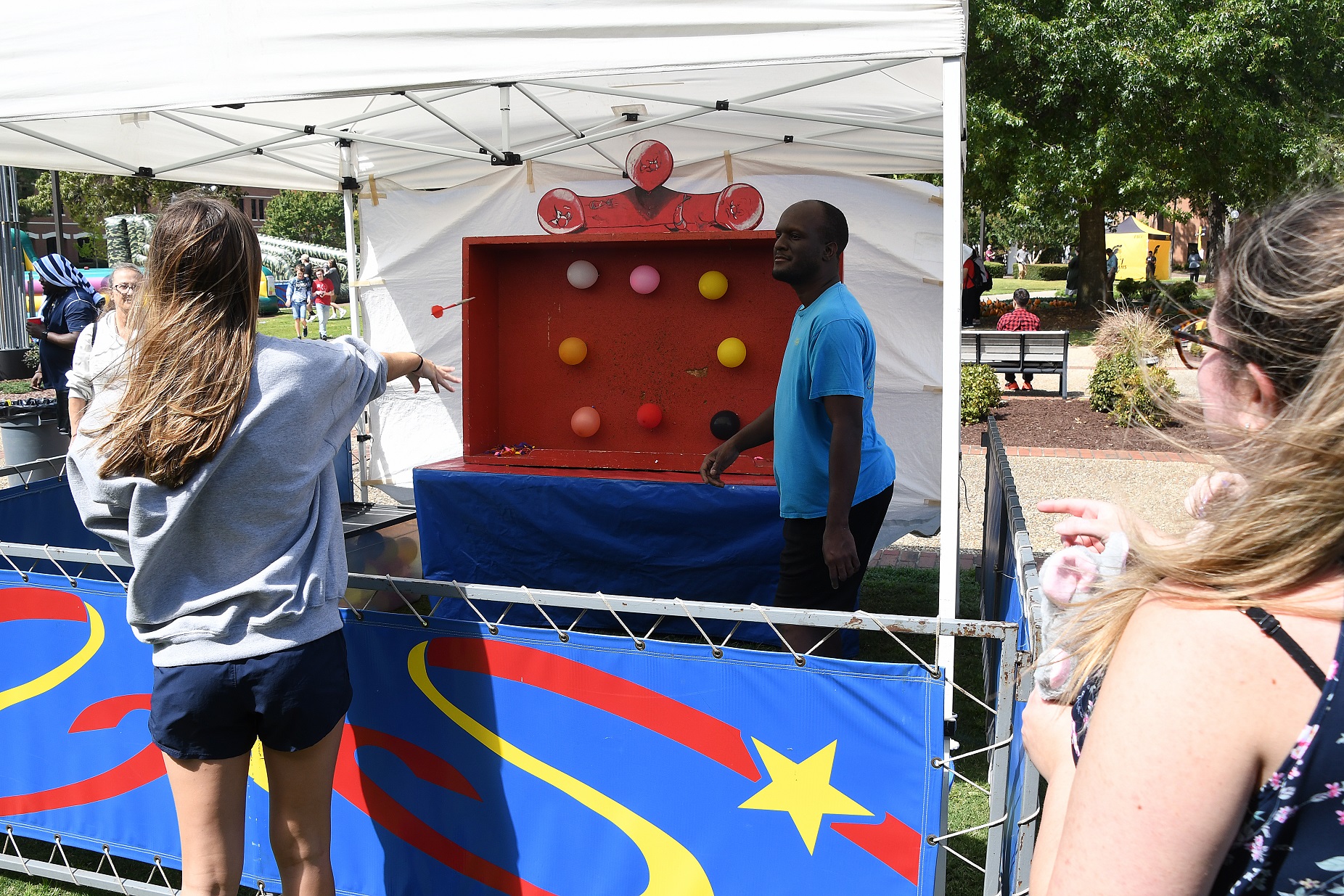 A student throws a dart at a board of balloons.