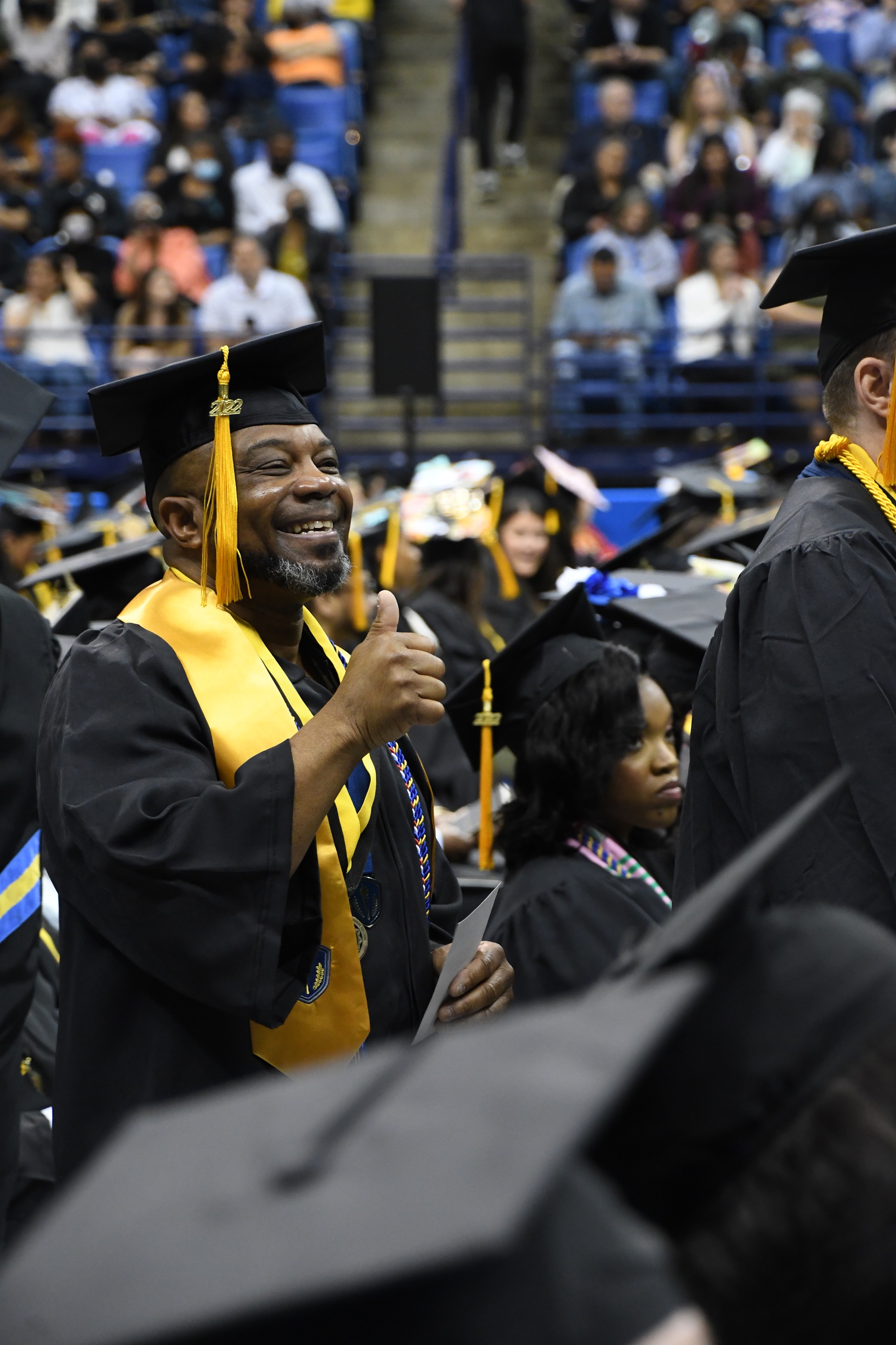 A graduate, wearing a wide gold stole, gives a thumbs-up to the crowd.