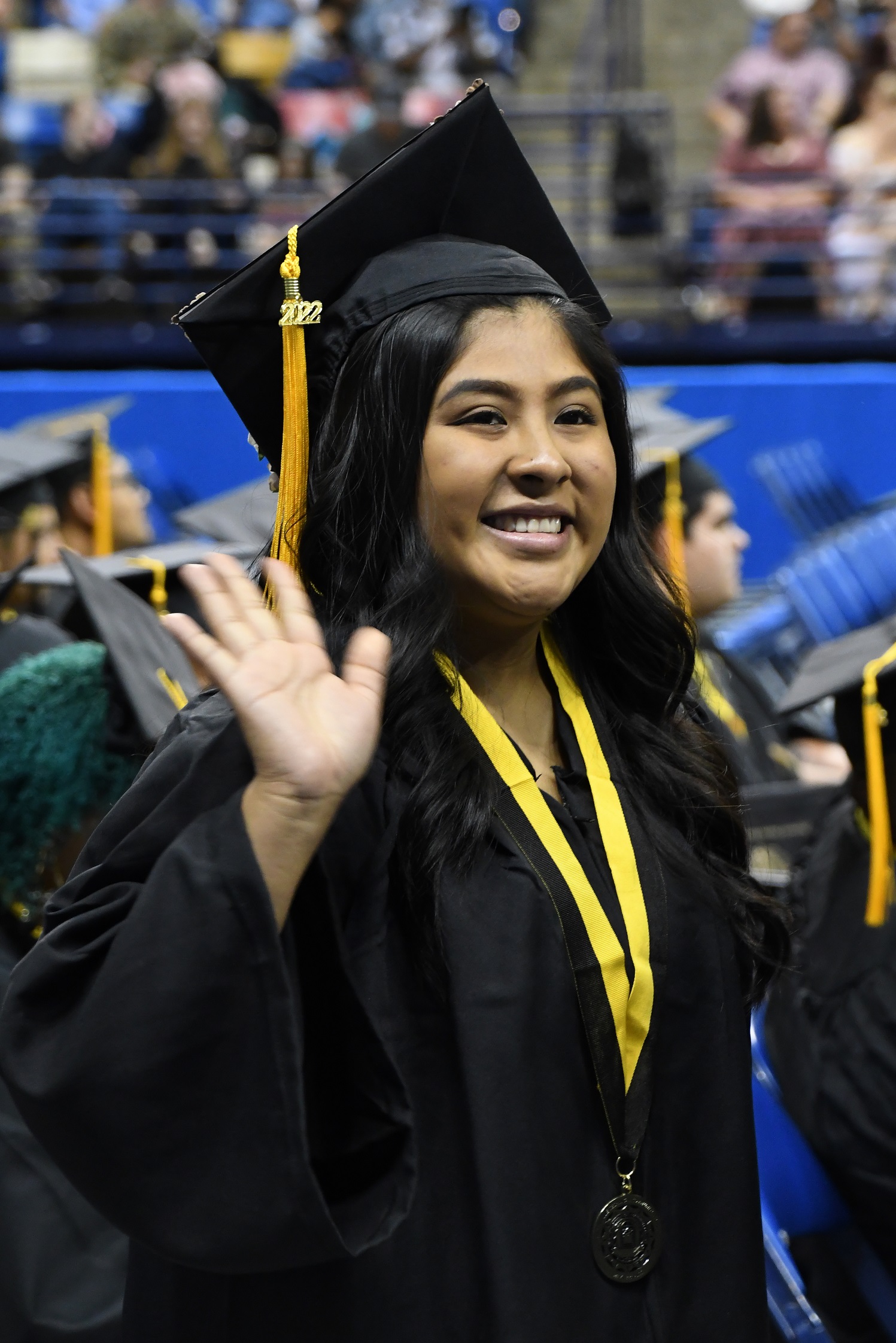 A smiling graduate waves to the crowd.