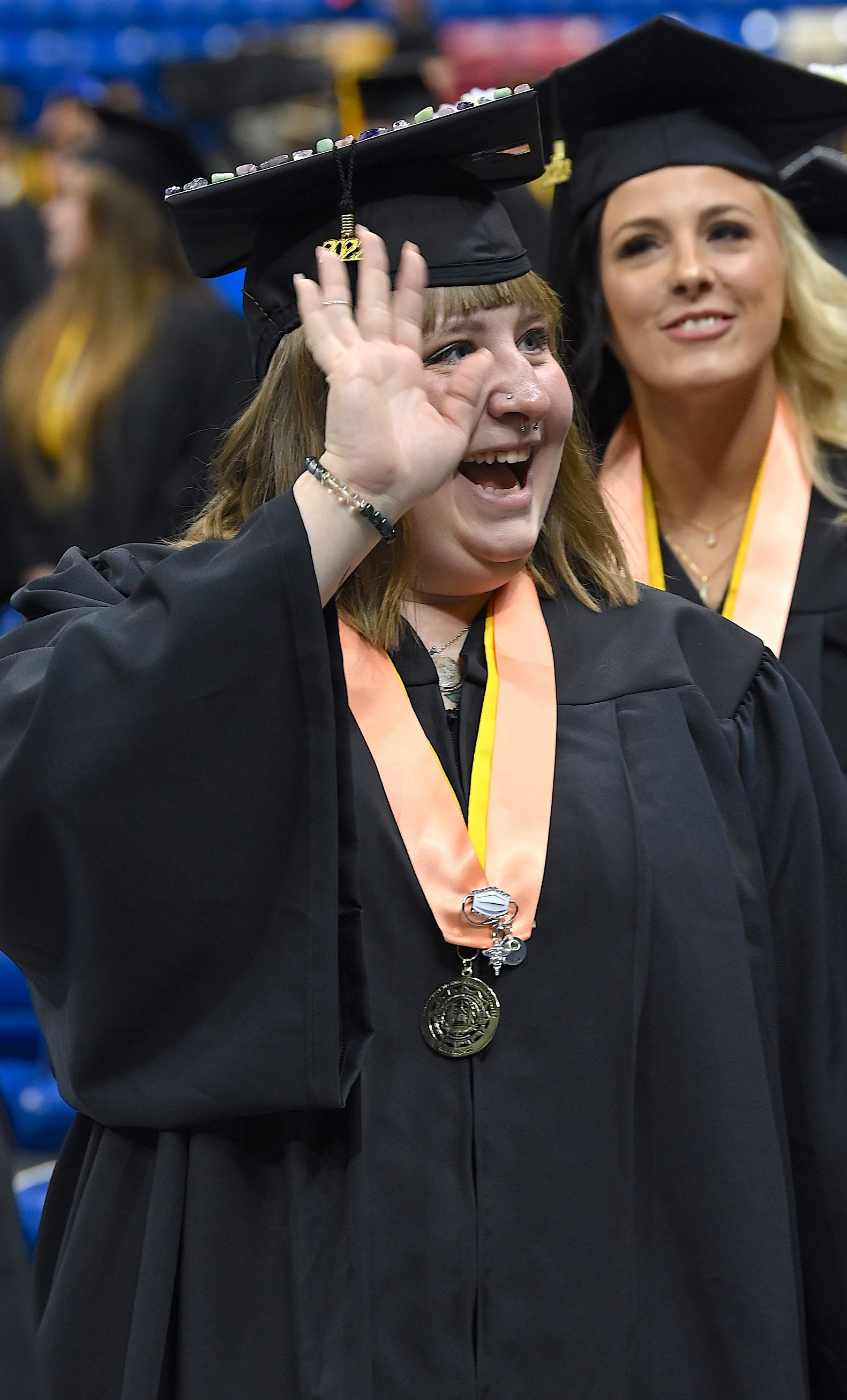 A graduate wearing a peach-color stole waves to crowd.