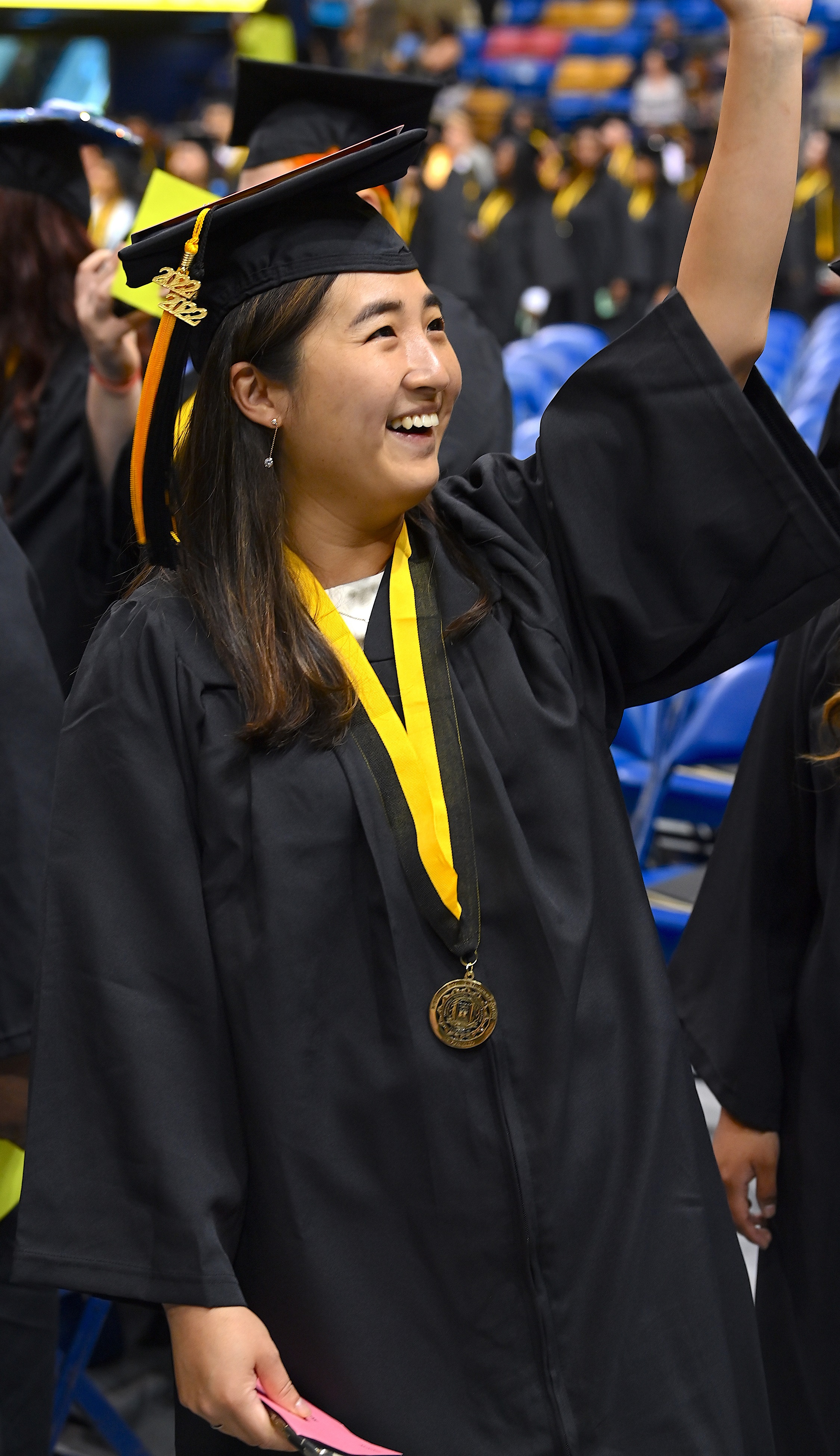 A smiling graduate raises her arm to wave to the crowd.