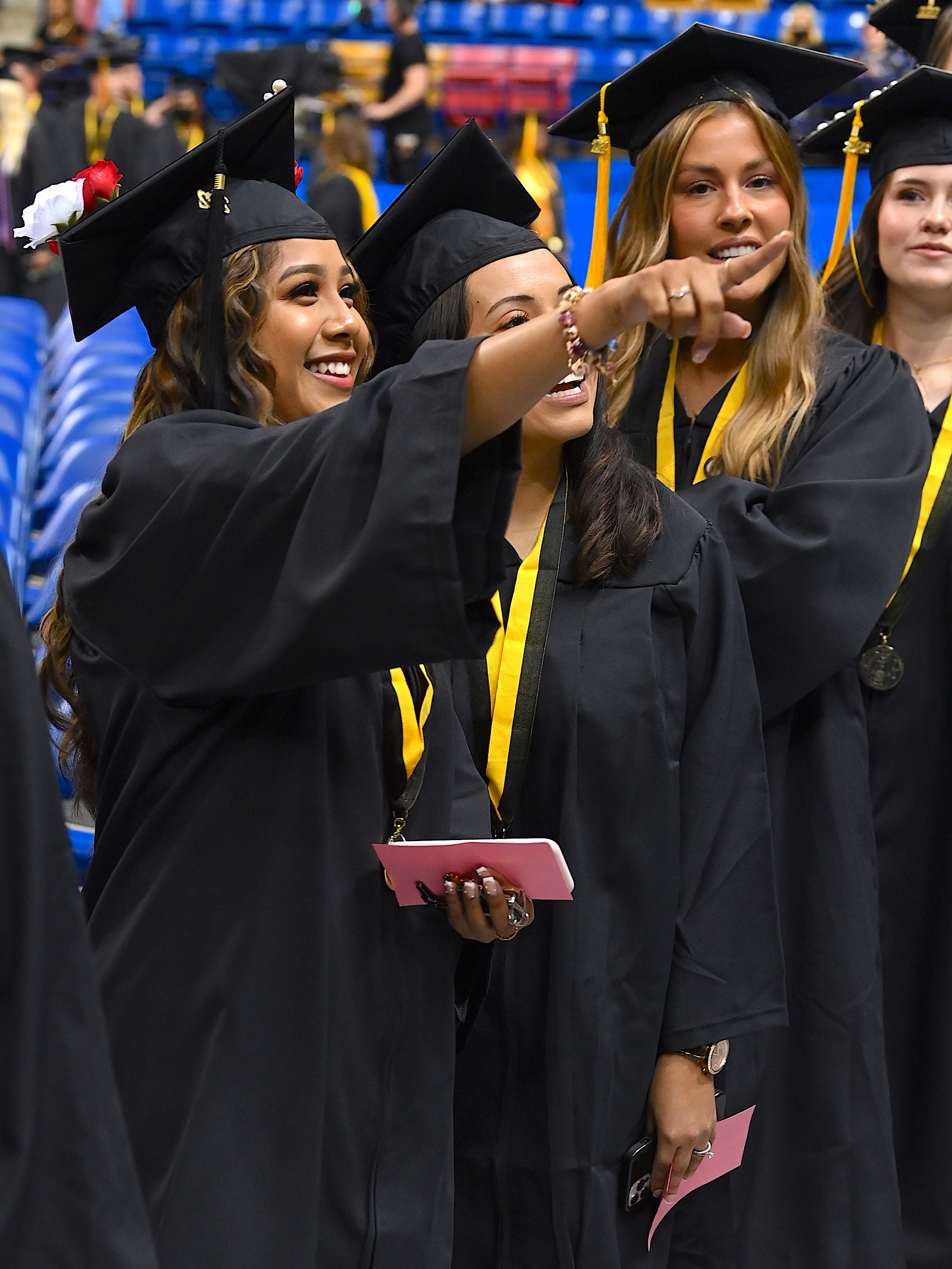 A graduate points to the crowd, showing the graduate behind her in line someone out of frame.