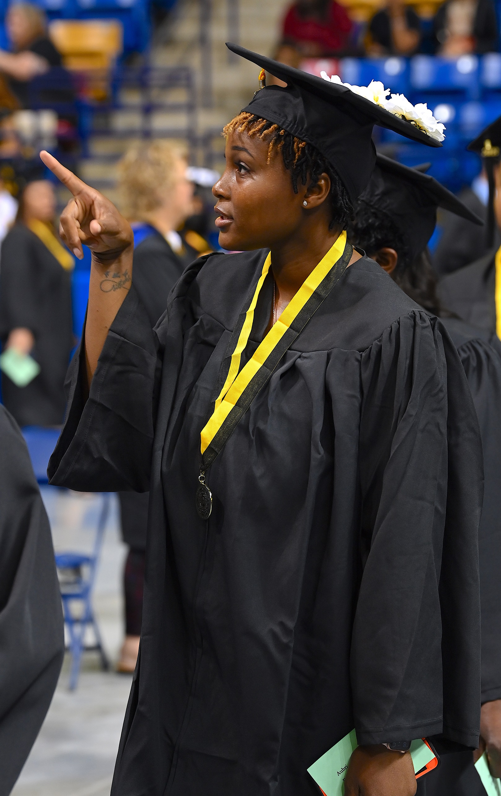 A graduate, photographed in profile, points up into the crowd.