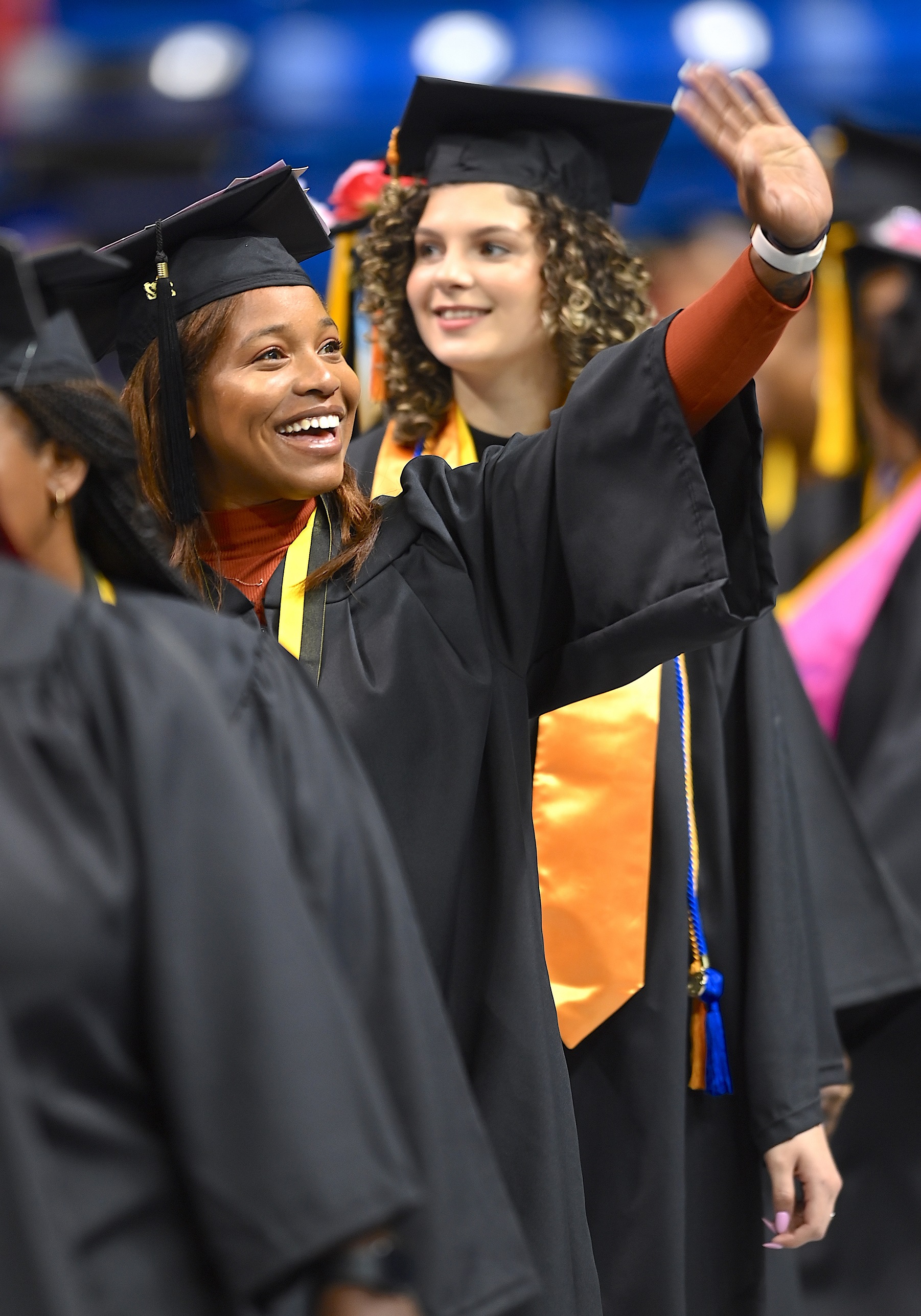 A graduate smiles and raises her hand to wave to the crowd.
