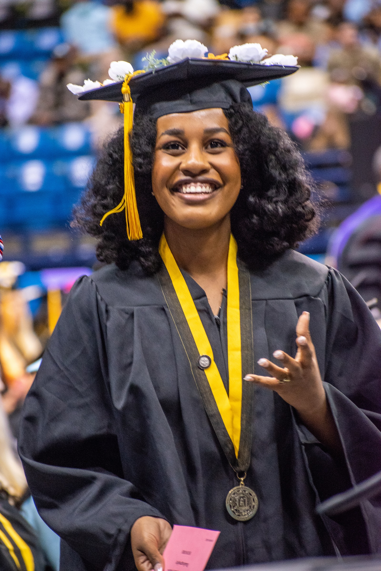 A graduate raises her hand with the palm up and smiles up at the crowd.