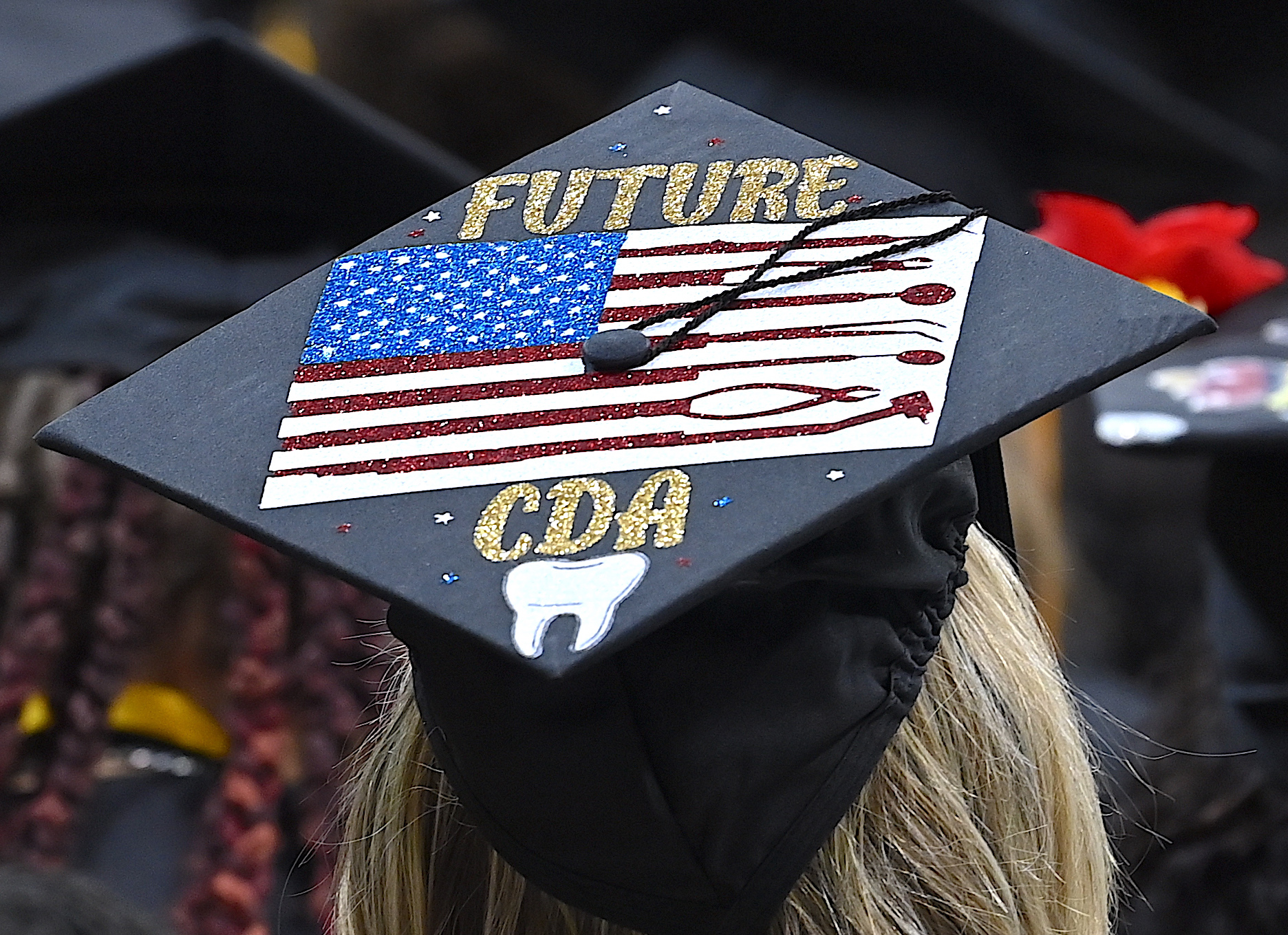 A graduation cap decorated with the flag of the United State. The cap says "Future CDA" and has a white tooth drawn on it."
