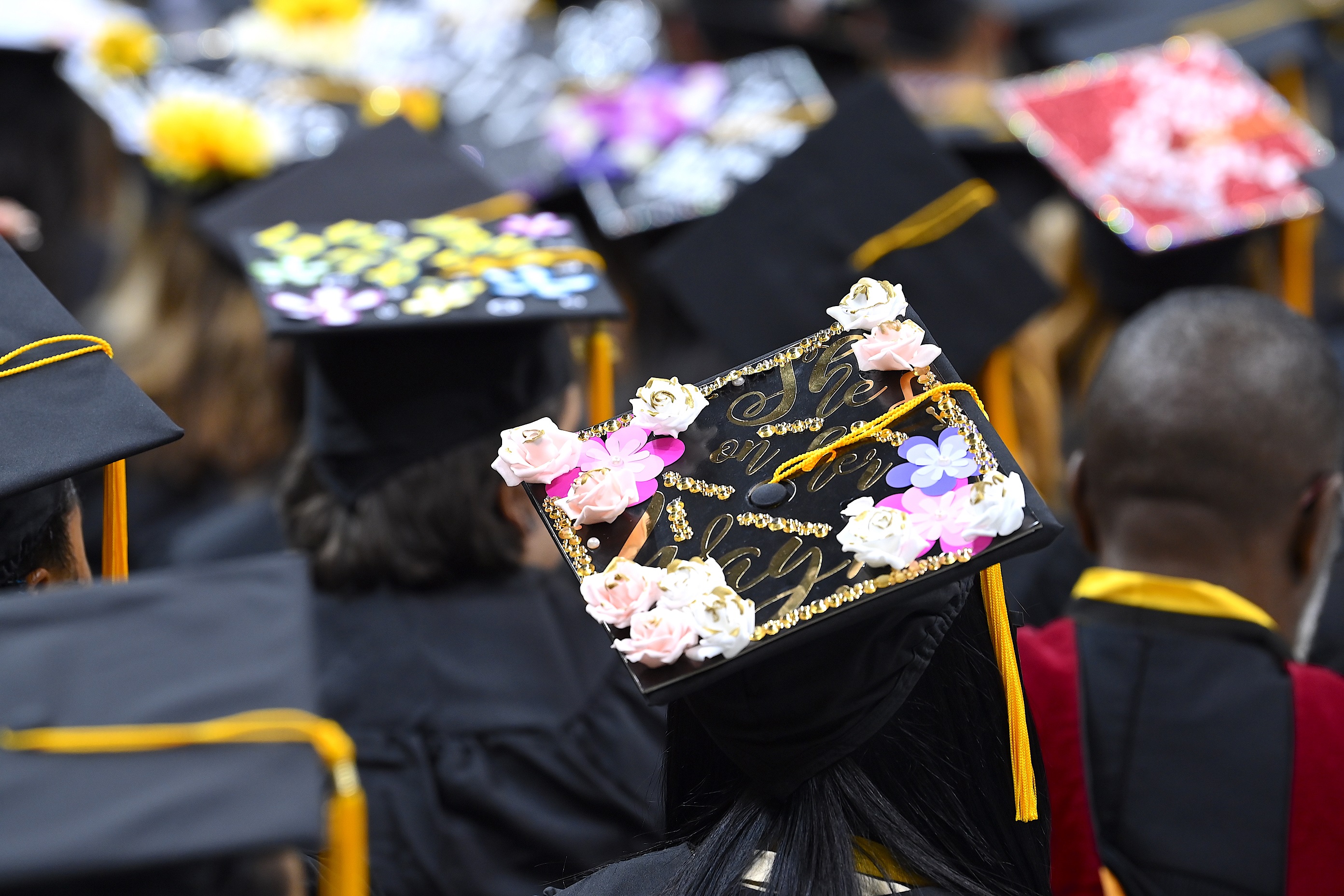 A graduation cap decorated with flowers and gold trim. It says "She's on her way."