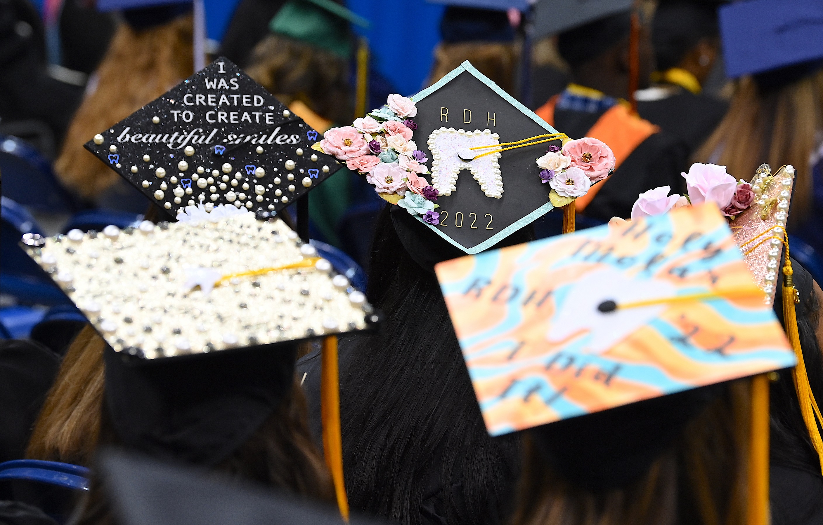 Graduation caps in focus in the background of the photo. The cap on the left says "I was created to create beautiful smiles." The cap on the right says "RDH 2022" with a paper tooth on it."