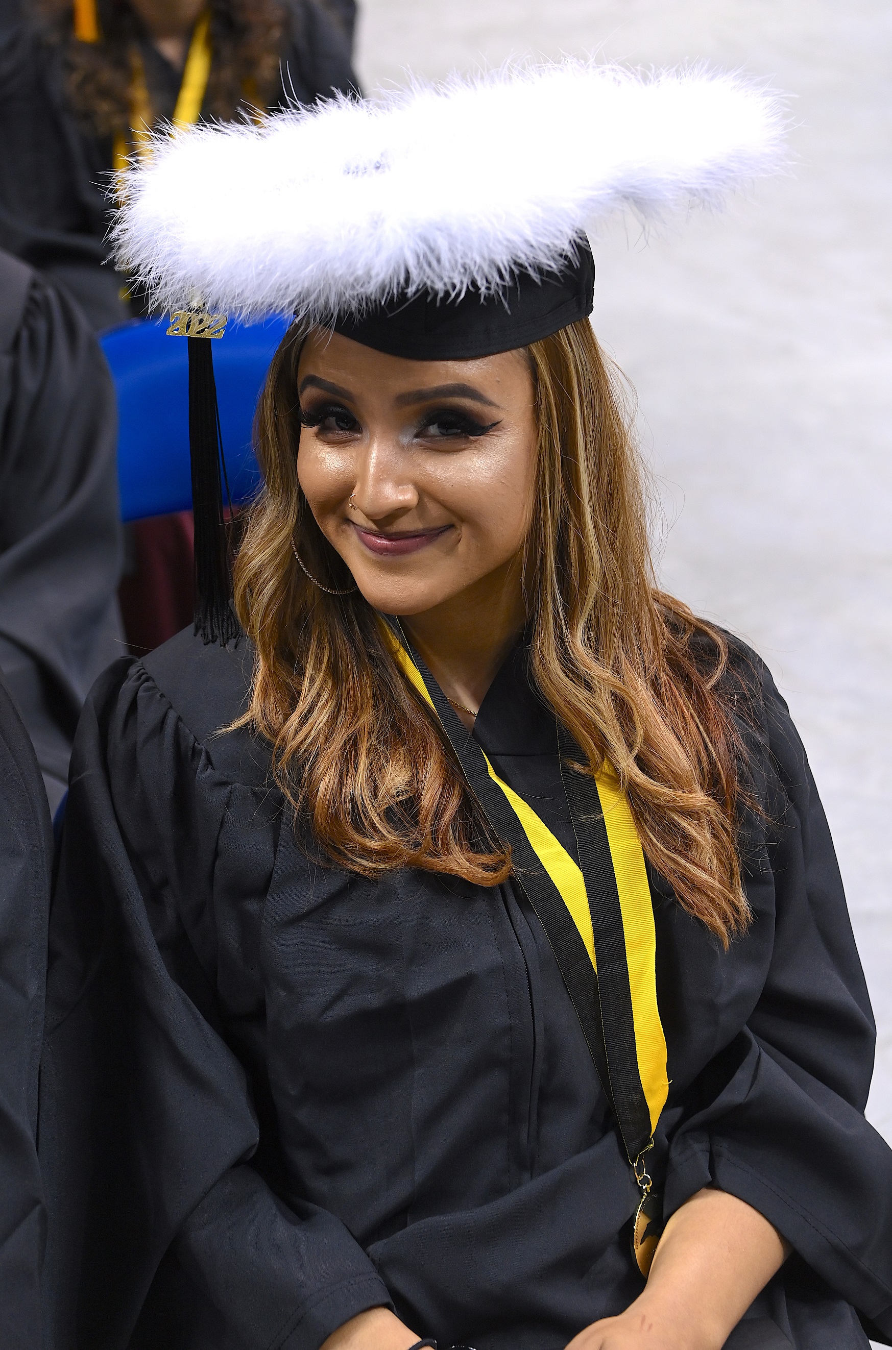 A graduate smiles at the camera from underneath a cap decorated with white fur trim.