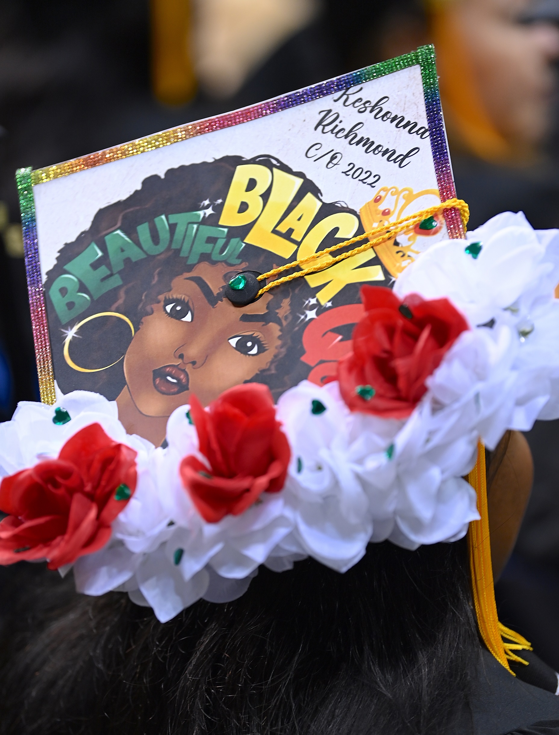 A graduation cap with silk flowers around the trim and an artist's drawing of a Black woman and the words "Beautiful. Black" written across the cap.